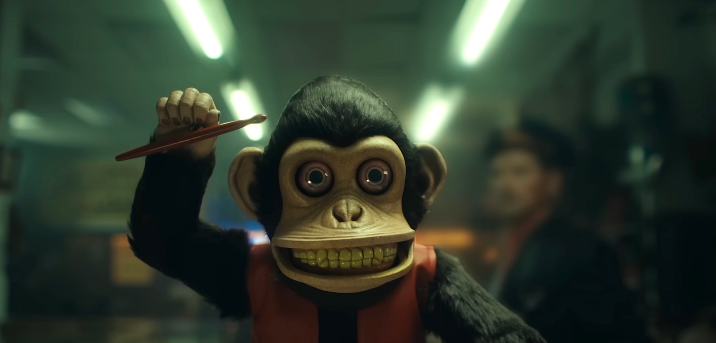 A grinning toy wind-up monkey with one drumstick raised in the air, from the trailer for Osgood Perkins’ The Monkey